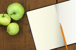 notebook with pencil and apples on a wood table