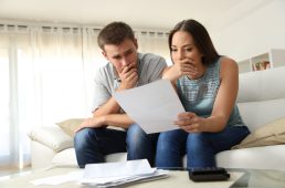 Worried couple reading a letter sitting on a couch in the living room at home