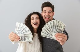 Image of rich man and woman holding fan of dollar money isolated over gray background